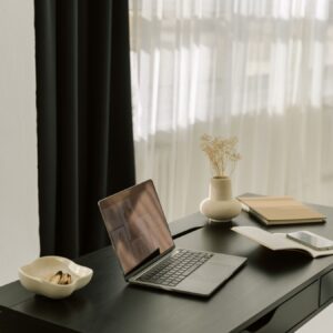 Stylowe biurko z laptopem, otwartym notesem, smartfonem i ceramiczną miseczką z przekąskami. Elegancka, uporządkowana przestrzeń sprzyja pracy zdalnej i organizacji codziennych obowiązków.