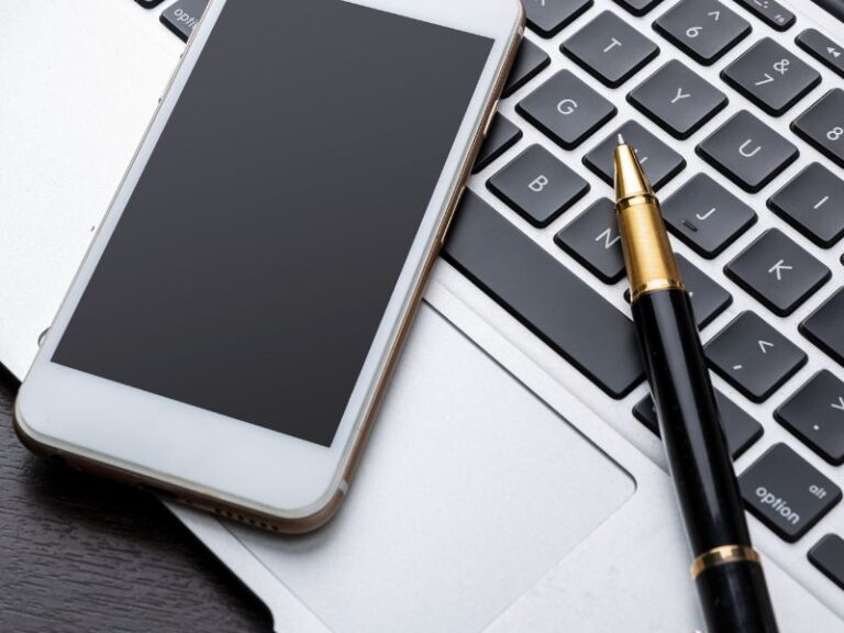 Laptop, telefon i notes na biurku – narzędzia do zarządzania czasem i planowania dnia